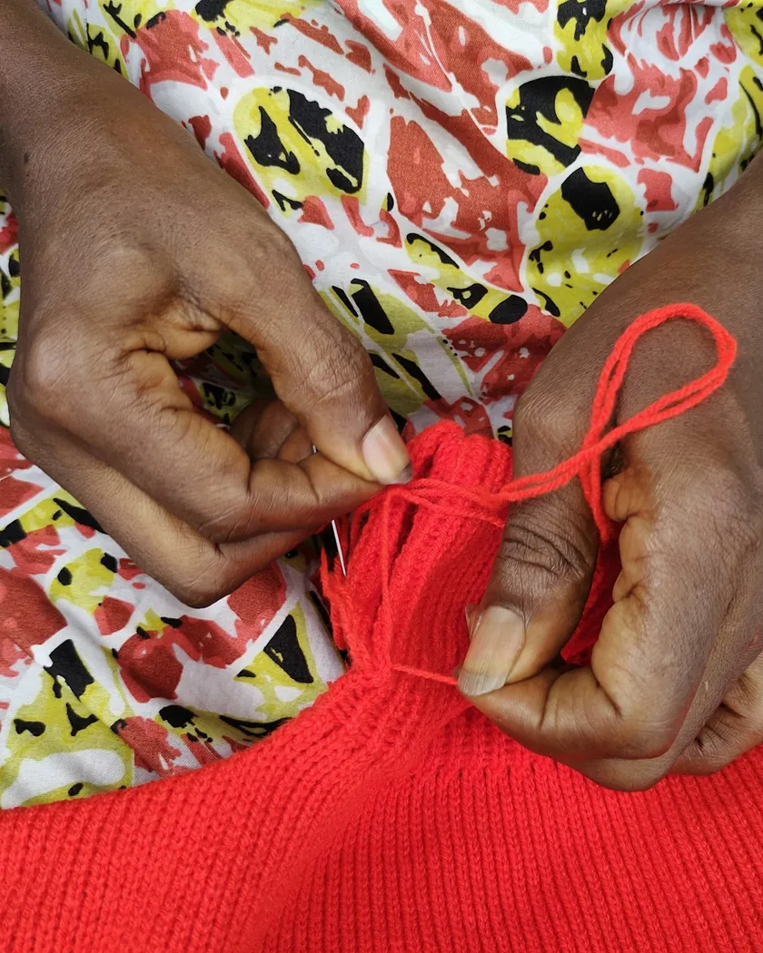Manos sosteniendo y enrollando hebras de lana roja sobre una labor textil en primer plano